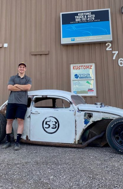Bare metal rat rod coupe with a painted number 53 on the door outside the shop