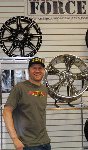 Shop staff member standing beside a display wall of custom truck wheels