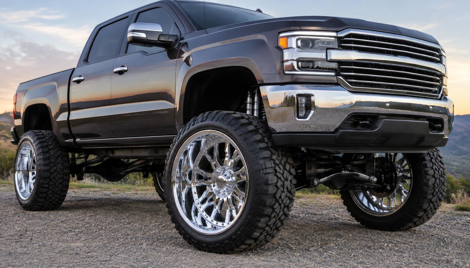 Polished chrome aftermarket wheels mounted on a lifted pickup truck at sunset
